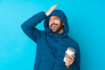 Man wearing winter jacket and holding a takeaway coffee over isolated blue background has realized...
