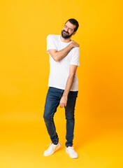 Full-length shot of man with beard over isolated yellow background suffering from pain in shoulder...