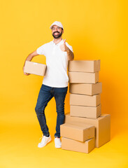 Full-length shot of delivery man among boxes over isolated yellow background with thumbs up because...