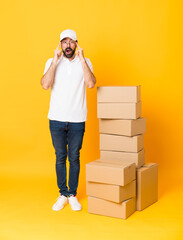 Full-length shot of delivery man among boxes over isolated yellow background with glasses and...