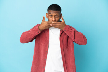 Young latin man isolated on blue background covering mouth with hands