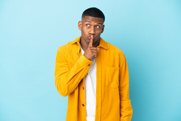 Young latin man isolated on blue background showing a sign of silence gesture putting finger in mouth