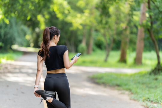 Healthy woman warms up before jogging and relaxes. Stretch your arms and look outside at the road, get in shape at the park before running and enjoy healthy outdoor activities.