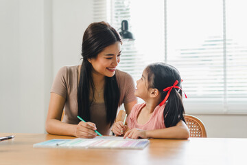 Young mother assists her daughter with coloring activities at a home desk during daytime.