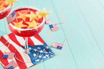 4th of July Holiday background. Cranberry punch with ice and stars shaped apple pieces in glass against background of old turquoise board and sun rays. Patriotic American Flag drinks. Mock up.