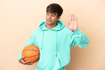 Handsome young basketball player man isolated on ocher background making stop gesture and...