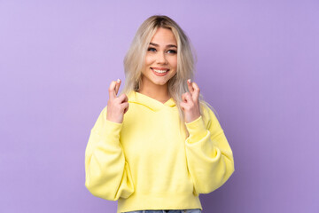 Teenager girl wearing a yellow sweatshirt over isolated purple background with fingers crossing