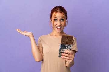 Teenager Russian girl isolated on purple background taking a chocolate tablet and surprised