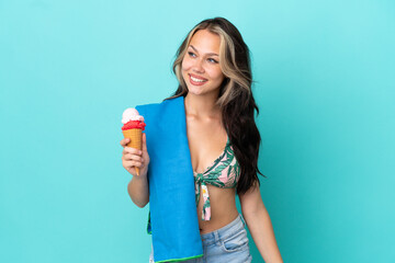 Teenager caucasian girl holding ice cream and towel isolated on blue background looking side