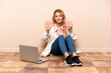 Teenager woman with a laptop sitting on the floor at indoors counting nine with fingers