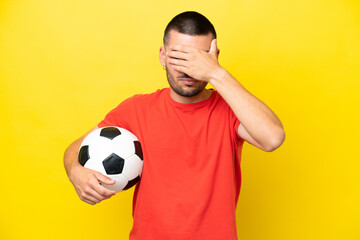 Young caucasian man playing soccer isolated on yellow background covering eyes by hands. Do not...