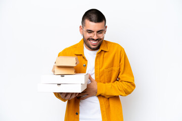 Young caucasian man holding pizzas and burgers isolated on background smiling a lot