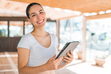 Young pretty woman at outdoors holding a tablet with happy expression