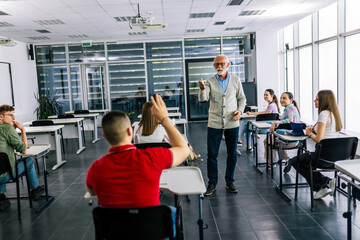Fototapeta premium Teacher calling on student with raised hands in education classroom