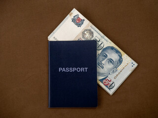 Fototapeta premium Singapore dollar money background. Blue passport with 50 Singapore dollars currency banknote isolated on wooden table background. Business finance and banking concept.