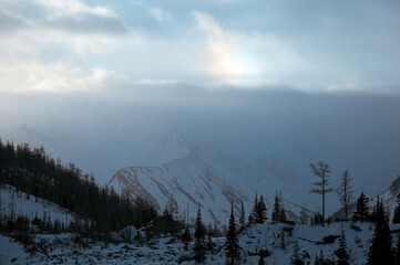 Sunlight breaks through clouds above snowcovered mountains.