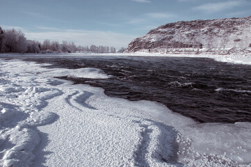 A frozen river bank with a distant mountain under a cloudy sky