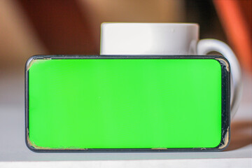 Green screen smartphone leaning on a cup on the table