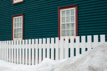 A dark green exterior wall of a historic house with two casement windows.  The trim around the...