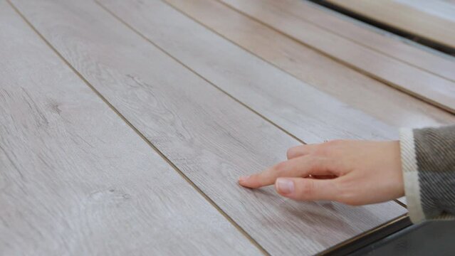 Woman choosing laminate flooring for her home in flooring store, woman's hand ironing new laminate while checking its structure in hardware store.
