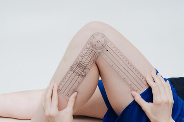 Female physiotherapist examining knee angle of patient with goniometer. on the background of a white wall in the hospital