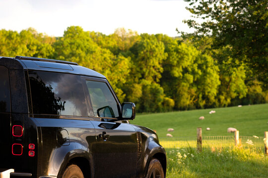 Gaydon, Warwick, UK June 2024: New Land Rover Defender Detail. Short wheel base 90 variant being used on farm with sheep field, vibrant green grass and sunset over trees. Agricultural countryside 4x4 