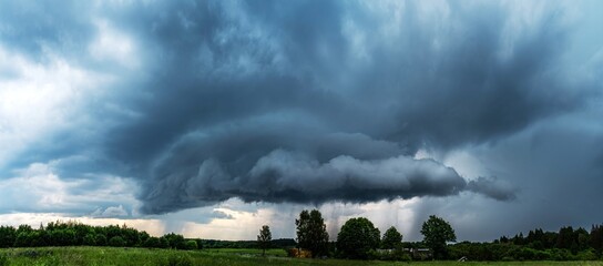 A huge, dark shelf cloud, storm cloud drifts across the meadow in Lithuania