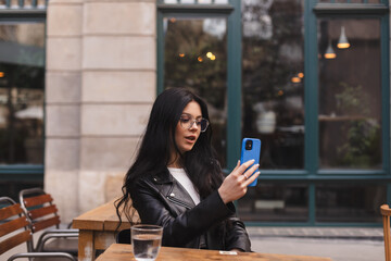 Calm teen girl using smartphone at cafe. Sensual brunette woman using smart phone make selfie,...