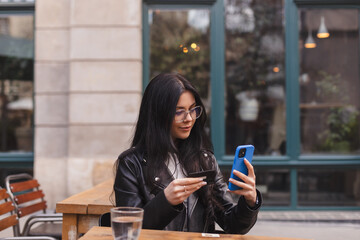 Happy young brunette woman customer shopper holding credit card using cell phone mobile app buying...