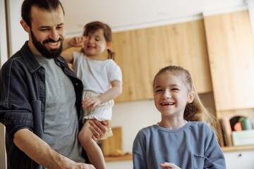 a father checking his 6-year-old daughter's homework, a girl sitting at the kitchen table doing her homework in front of her father who is cooking in the kitchen