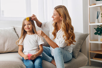 Mother and daughter bonding time woman gently combing her child's hair on cozy living room couch