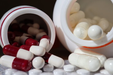 white or white medicine capsules and spilling out of container lying on the table