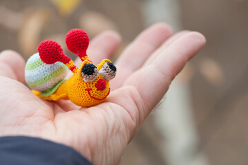 Textile handmade funny happy snail toy in hand on natural blurry background. macro photo. multi-colored snail. beautiful toy, close-up. the concept of childhood, games, education