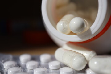 white or white medicine capsules and spilling out of container lying on the table