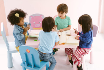 Cute group Diverse little children sitting on table in art class at kindergarten with talking something while drawing with colored pencil in notebook. Children and education concept.