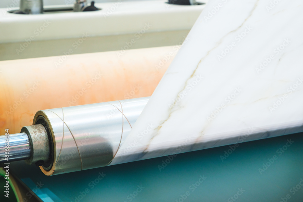 Aufkleber A roll of white paper is being fed through a machine. The machine is in a factory setting