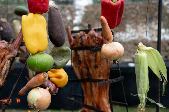 Verduras cocinandose a la llama, colgadas, de fondo desenfocado carne en parilla vertical