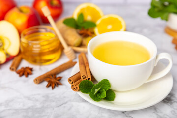 Fragrant hot tea with cinnamon stick and anise on a textured wooden background. A cup of hot tea with honey, lemon, mint and apples. Spicy tea with spices. Immunity tea. Health concept.Copy space.