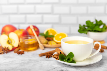Fragrant hot tea with cinnamon stick and anise on a textured wooden background. A cup of hot tea with honey, lemon, mint and apples. Spicy tea with spices. Immunity tea. Health concept.Copy space.