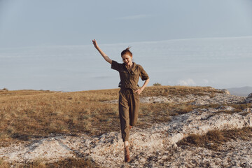 Young woman jumping on rock in field with hands in air, enjoying travel adventure and nature beauty