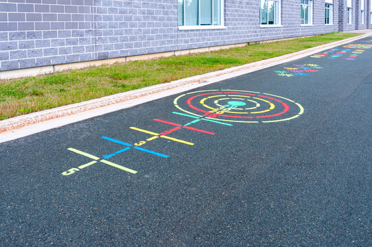 A children's playground ring toss game painted on black pavement. There are yellow, red, and green color circles and lines drawn on the ground. The activity is next to a grey brick school building.
