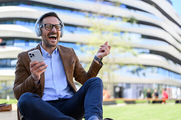 Ecstatic businessman with eyes closed enjoying music over headphones while sitting against building