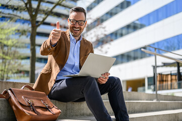 Portrait of successful male professional with laptop showing thumbs up sign while sitting on steps