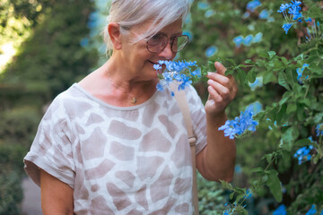 Smiling senior Caucasian woman smells a blue flower outdoors in the garden. Spring, summer and nature awakening