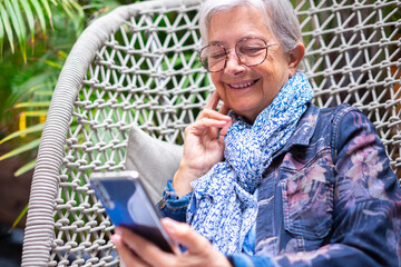 Portrait of smiling relaxed senior woman using mobile phone reading a message sitting on armchair....