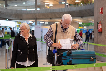 Senior travelers couple with suitcases pushing luggage trolley while walking through airport area...