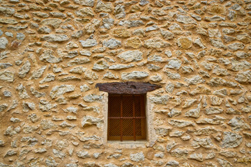Beige stone brick wall made of sandstone with a window with wooden lintel and metal safety grill. 
Such the walls are usual in Mallorca, Spain