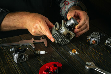 Hands of a craftsman on a work table in a workshop repairing a trimmer engine. Replacing the engine...