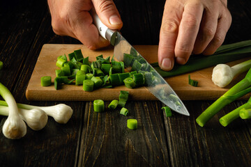 Chef hands chop green garlic with a knife on a cutting board for vitamin salad. Diet menu for...