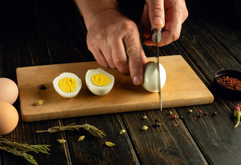 A cook uses a knife to slice boiled eggs on a wooden board before preparing dinner. Advertising...